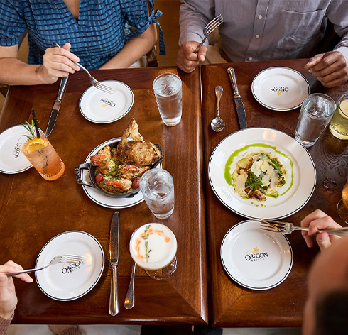 A top down view of a restaurant table with plates of vibrant food and various cocktails.