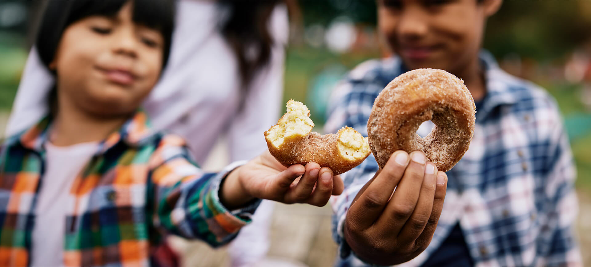 Children holding cinnamon-sugar apple cider donuts during a fall farm visit in Baltimore County