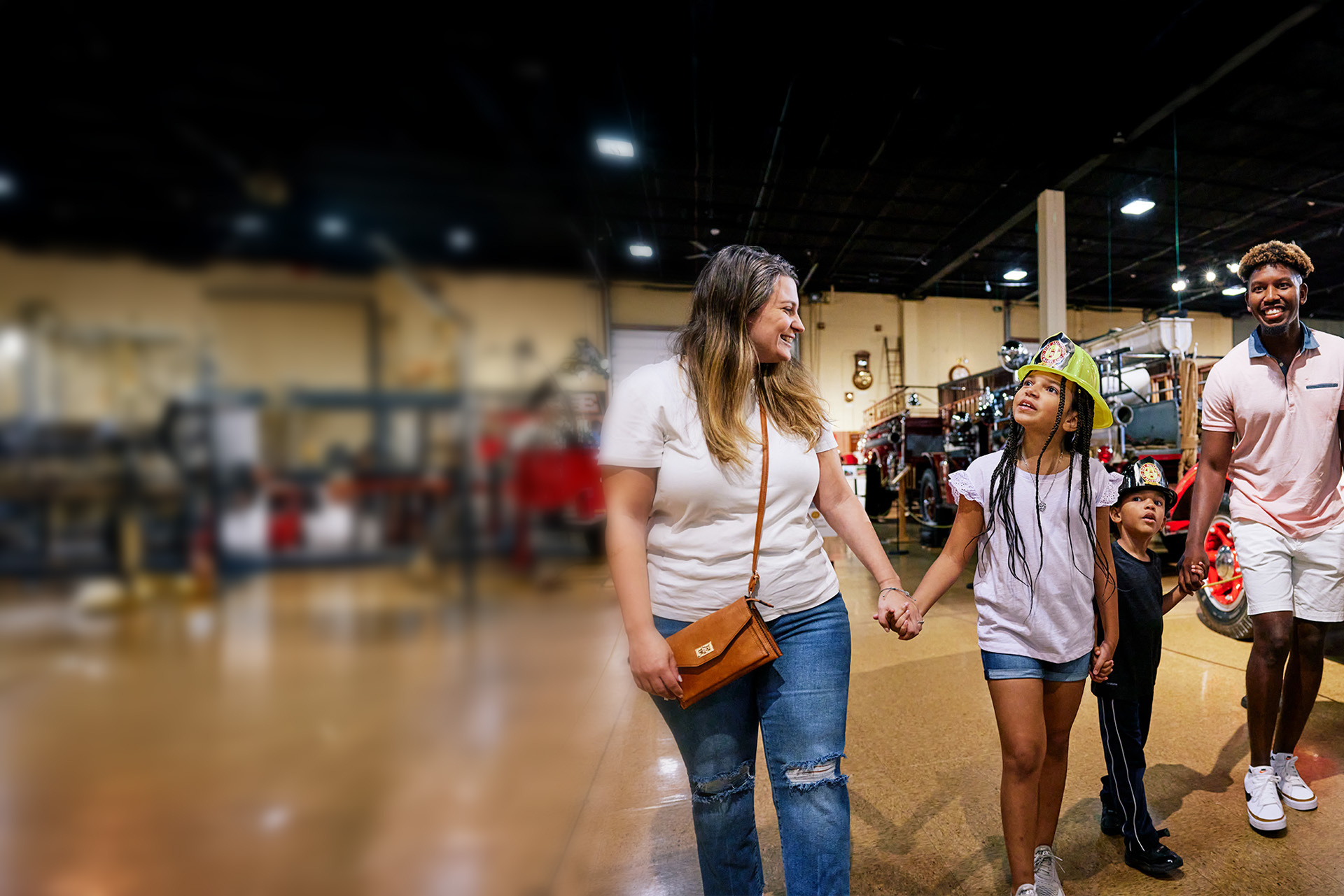 A family of four walking through the fire museum in Baltimore County, while smiling and holding hands. The left side of the image is blurry.